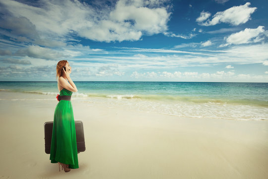 Beautiful woman traveler at the beach with suitcase talking on mobile phone
