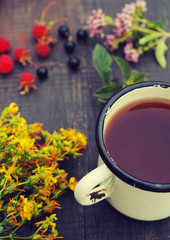 Tea in an iron mug, medicinal herbs and juicy berries on a wooden surface.
