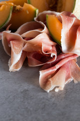 Jambon mix. Ham. Traditional Italian and Spanish salting, smoking, dry-cured dish - jamon Serrano and prosciutto crudo sliced with melon on grey background. Copy space. Closeup. 
