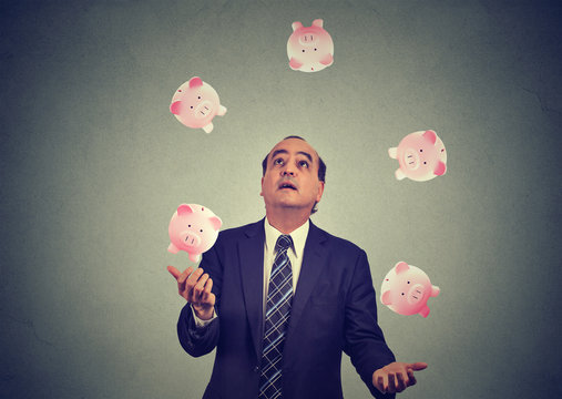 Middle aged business man juggling money piggy bank