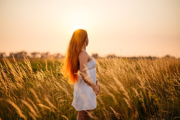 Obraz premium Young beautiful red-haired girl in a field at sunset