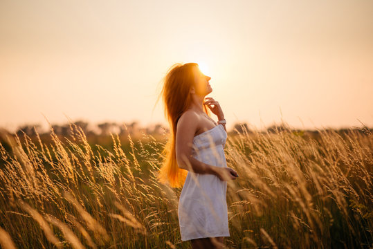 Young beautiful red-haired girl in a field at sunset