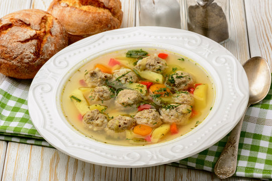 Soup with meatballs on white wooden background.