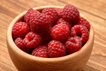 Ripe raspberries in wooden bowl. Close-up.