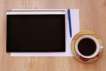 Office workstation, Cup of coffee , tablet and white papers the table. The table of a businessman, a businesswoman. The view from the top.