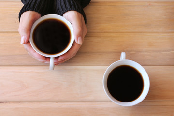 Female hands holding a Cup of coffee and standing next to another Cup of coffee on a rustic wooden table as background.