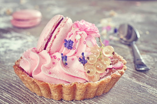 Vintage toned dessert tart with pink meringue and white currants on wooden table.