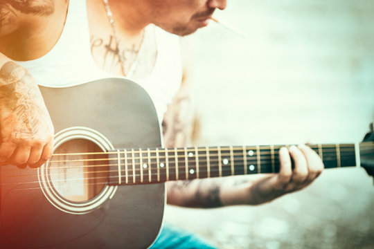 Hipster  with tattoos playing guitar. Lens flare added.