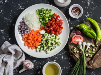 Fresh chopped vegetables - tomatoes, zucchini, carrots, tomatoes, onions, peppers on a dark background. Ingredients for ratatouille. Top view