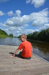 Kind sitz auf Bootssteg am Fluss und beobachtet die Strömung