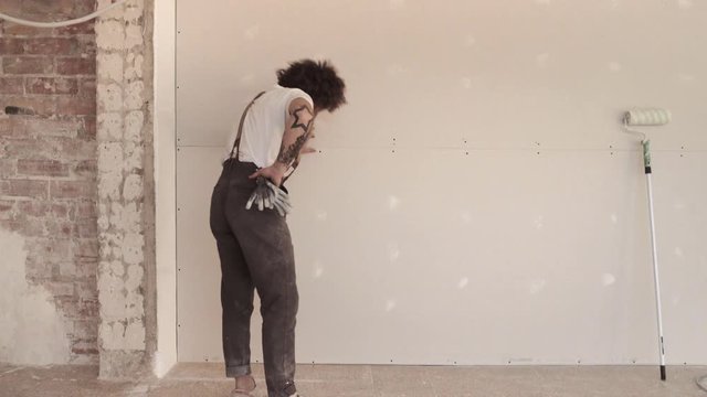 Funny curly man wears pants with suspenders checking the quality of plasterboard wall building works, shakes with his head positively and goes out