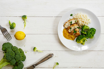 fried chicken breast fillet with a fruity sauce, broccoli and rice, top view from above on white wood
