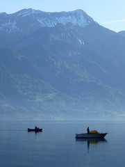 Two small fishing boats on Brienzersee Lake, Switzerland in early morning hazy sunshine, with the snow covered peak of the Rothorn mountain rising up behind