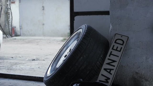 Car wheel and lisence plate named wanted in the garage where girl legs appear