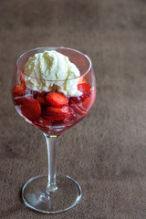 Sliced strawberries and vanilla ice cream in a wine glass on a brown background
