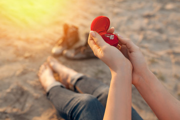 female's hand hold gift box with golden engagement ring;