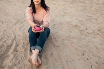 barefoot female on the beach and with cup of coffee;