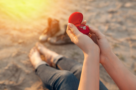 female's hand hold gift box with golden engagement ring;