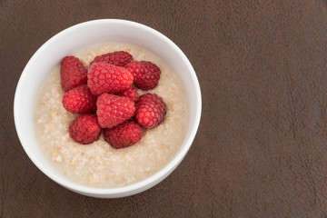 Fresh picked raspberries topping oatmeal in a white bowl, top view
