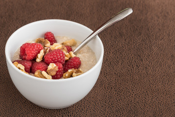 Spoon dipping into fresh picked raspberries and walnuts topping oatmeal in a white bowl
