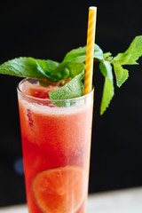 Raspberry-chocolate black tea with ice in a glass beaker on a wooden table over dark background