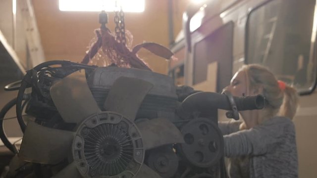 Girl in jeans rummaging in the naked engine suspended in the garage