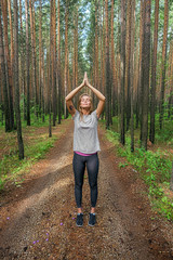 Calm meditating girl in forest with raised arms in namaste