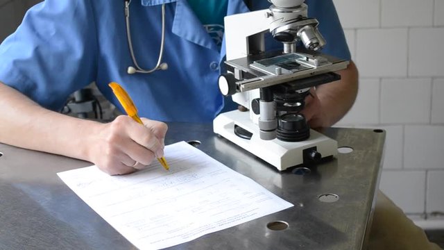 doctor looking into a microscope and writing on paper