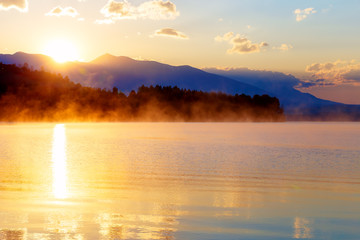 Naklejka premium beautiful landscape with mountains and lake at dawn in golden, blue and purple tones.
