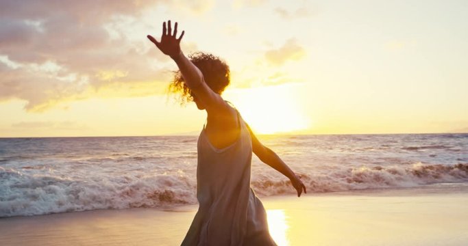 Beautiful young woman in sundress spinning on the beach at sunset in slow motion