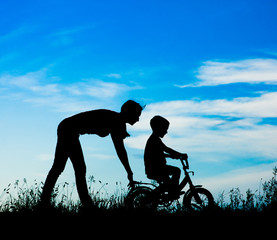 Fototapeta premium silhouette of a mother who teaches his son to ride a bike