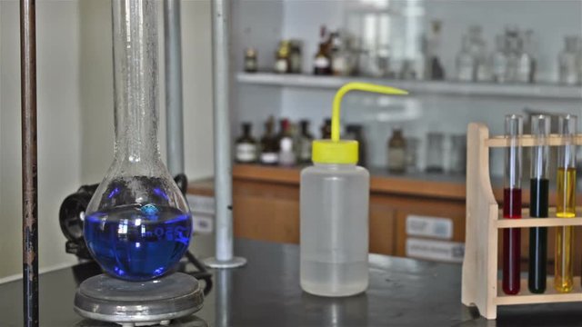 Boiling of blue liquid in a laboratory experiment. Several test tubes with colorful liquids and bottle beside.