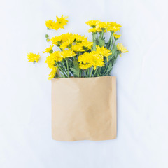 Yellow flowers and paper bag on white background. Flat lay, top