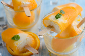 Homemade frozen ice cream popsicles made with oragnic fresh oranges on wooden background