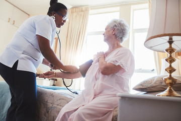 Female nurse checking blood pressure of a senior woman