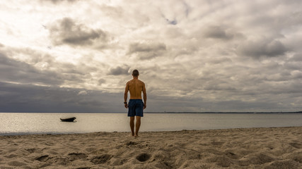 Fototapeta na wymiar Sporty man walking at the beach, boat on the ocean