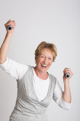 femme s&eacute;nior riant en tenant des halt&egrave;res