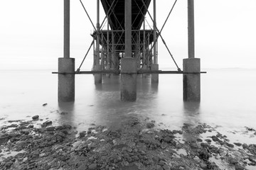 The underside of a pier with the sea sofened by a long exposure time - black and white