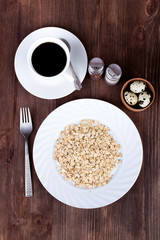 Dietary breakfast: quail eggs, oatmeal, hot drink on a wooden table. Flat lay.