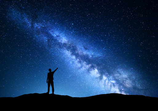 Milky Way. Silhouette of a standing man pointing finger in night starry sky on the mountain. Colorful night landscape with beautiful universe. Travel background with blue sky full of stars 