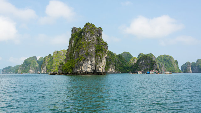 Big cliffs rising from the sea with small floating fishing village in Halong bay