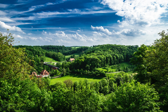 Taubertal nahe Rothenburg ob der Tauber. Gr&uuml;ner Wald und blauer markanter Himmel umrahmen alte sch&ouml;ne Geb&auml;ude.
