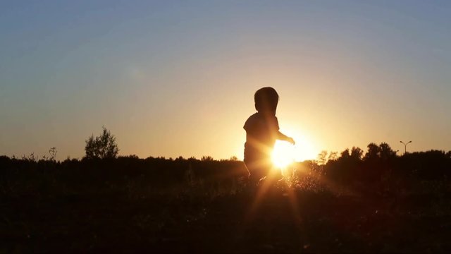 A little 1 year old baby boy is walking on sunset in nature. Child make his first steps outdoor. Kids Silhouette in the field with sundown