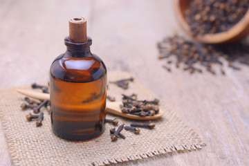Essential aroma clove oil in a glass bottle with dried cloves on wooden spoon and background.