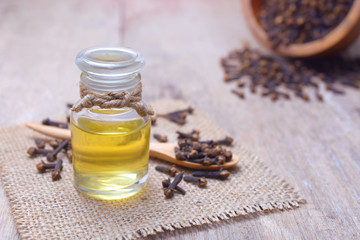 Essential aroma clove oil in a glass bottle with dried cloves on wooden spoon and background.