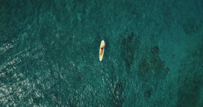 Aerial view of young man stand up paddle boarding on blue ocean waves
