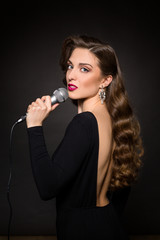 Portrait of beautiful lady singing in studio. Professional model with long brown hair posing in black dress over black background.