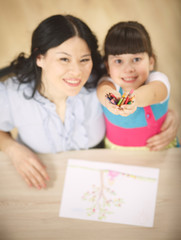 Top view of happy mother and her daughter looking at camera while sitting at atble and drawing pictures with multicoloured pencils.