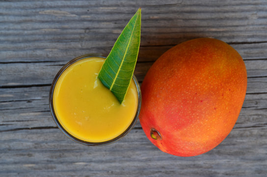 Fresh mango smoothie,ripe mango fruit and mango tree leaf on old wooden table background.Healthy food,diet or vegan food concept.Top view.