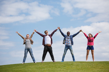 Picture of happy men and women with their hands raised smiling for camera while posing isolated on blue sky and white clouds.